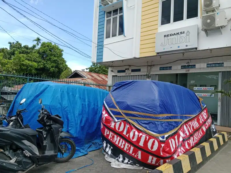 Dua mobil operasional Jubi yang rusak ditutupi terpal karena terbakar akibat serangan bom molotov ke kantor redaksi Jubi, pada Rabu, 16 Oktober 2024. - Jubi/Theo Kelen.